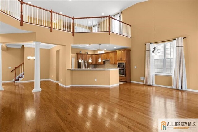 unfurnished living room featuring ornate columns, a high ceiling, and light wood-type flooring