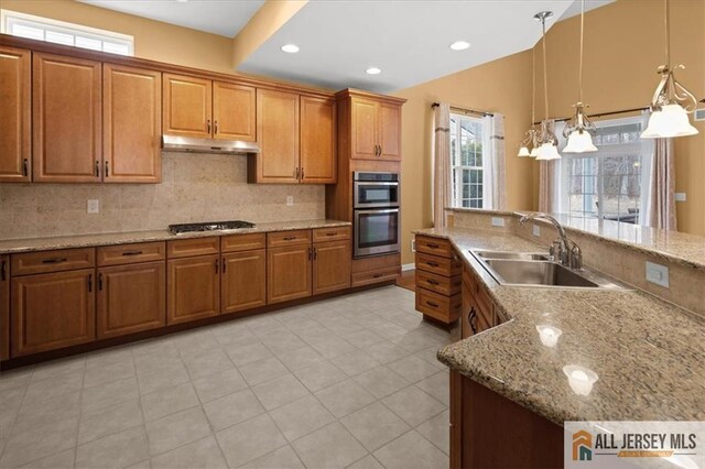 kitchen with pendant lighting, sink, gas cooktop, light stone counters, and stainless steel double oven