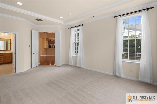 unfurnished bedroom featuring light colored carpet, ornamental molding, a tray ceiling, and ensuite bath