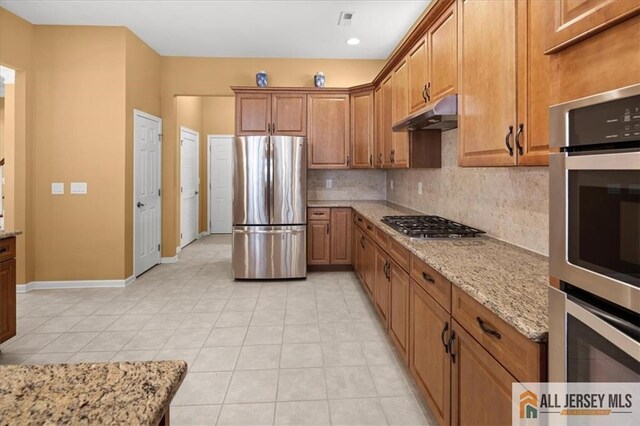 kitchen with appliances with stainless steel finishes, light tile patterned floors, backsplash, and light stone counters