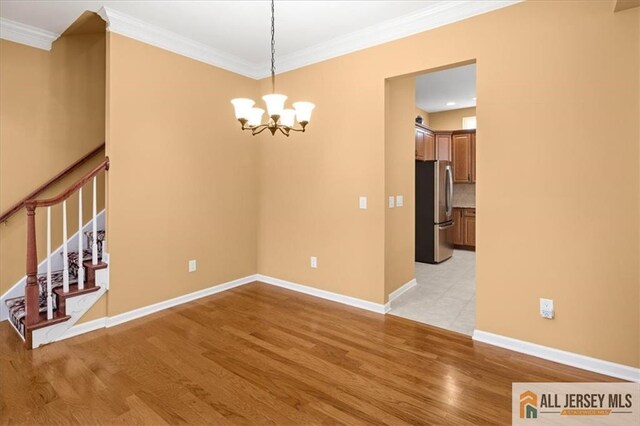 spare room with a notable chandelier, ornamental molding, and light wood-type flooring