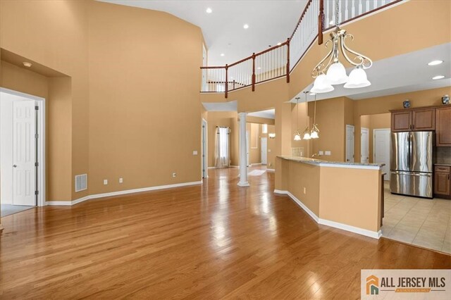 unfurnished living room featuring a towering ceiling, decorative columns, a chandelier, light stone counters, and light hardwood / wood-style flooring