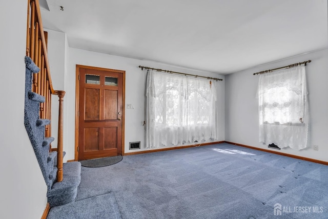 carpeted empty room featuring stairway and baseboards