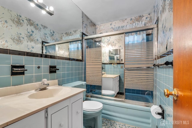 bathroom with wallpapered walls, tile walls, toilet, vanity, and enclosed tub / shower combo