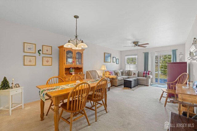 dining space with ceiling fan with notable chandelier and light carpet