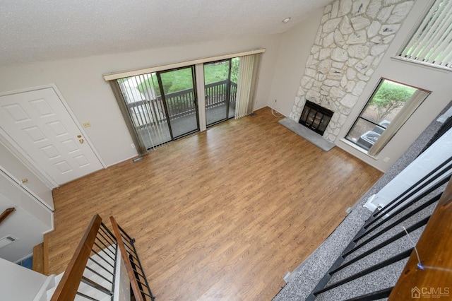 living room with vaulted ceiling, a stone fireplace, a textured ceiling, and light hardwood / wood-style floors