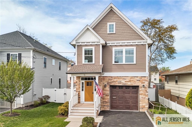 craftsman-style home featuring stone siding, an attached garage, a gate, driveway, and board and batten siding
