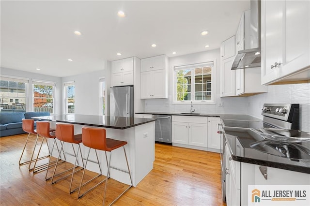 kitchen with appliances with stainless steel finishes, a sink, a breakfast bar area, light wood-type flooring, and recessed lighting
