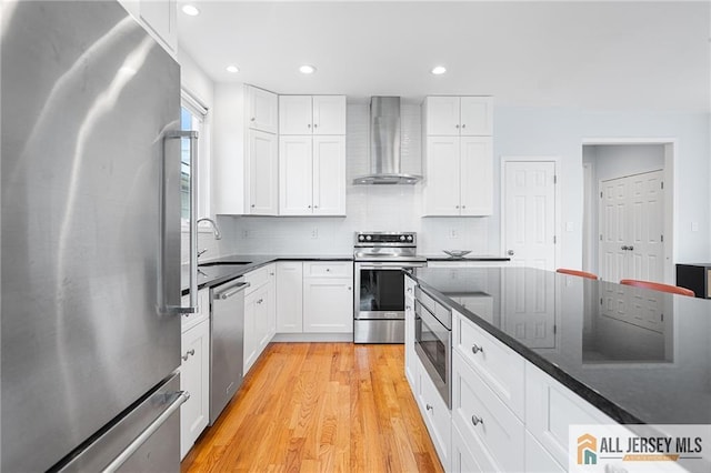 kitchen featuring appliances with stainless steel finishes, wall chimney range hood, a sink, light wood-type flooring, and backsplash