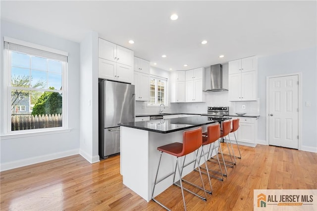 kitchen featuring freestanding refrigerator, wall chimney exhaust hood, a sink, a breakfast bar area, and white cabinets