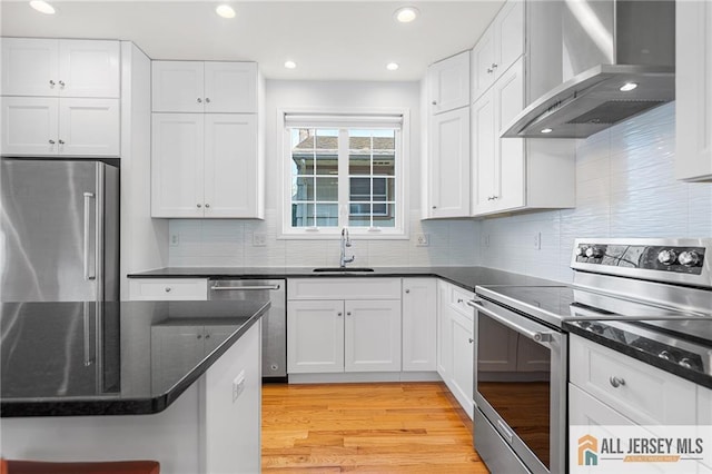 kitchen with stainless steel appliances, wall chimney range hood, a sink, white cabinetry, and light wood-style floors