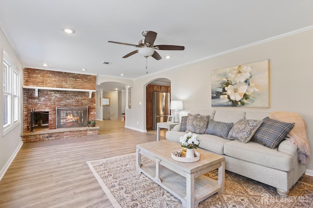 living room featuring a fireplace, ceiling fan, crown molding, and light hardwood / wood-style floors