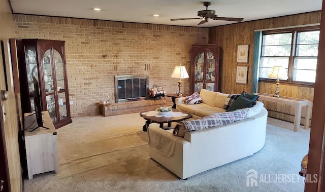 carpeted living area with brick wall, a brick fireplace, a ceiling fan, and wooden walls