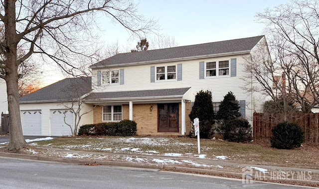 view of front of property featuring brick siding, roof with shingles, fence, a garage, and driveway