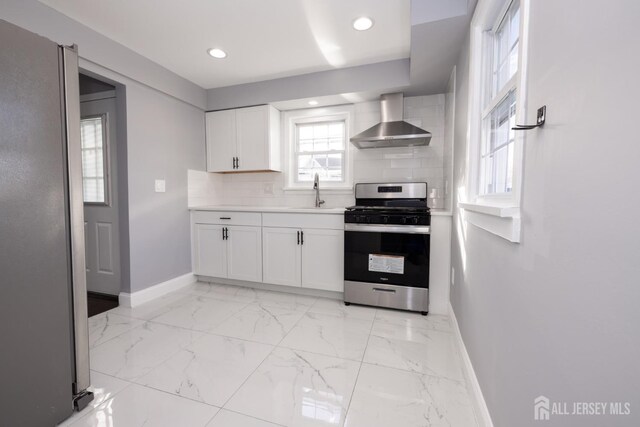 kitchen with sink, appliances with stainless steel finishes, white cabinets, wall chimney range hood, and backsplash