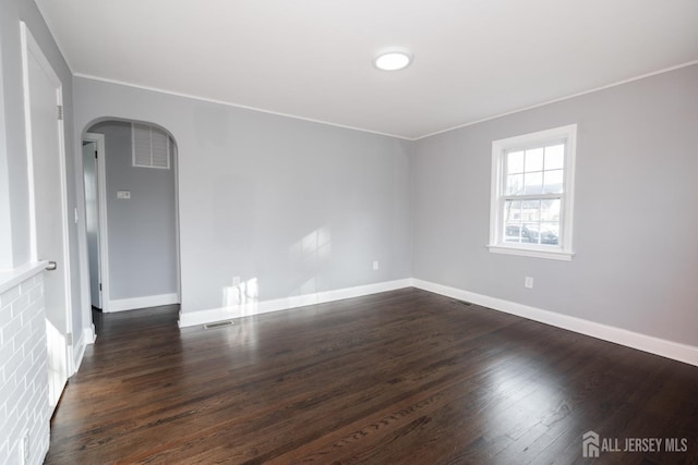 unfurnished room with arched walkways, dark wood-type flooring, visible vents, baseboards, and crown molding