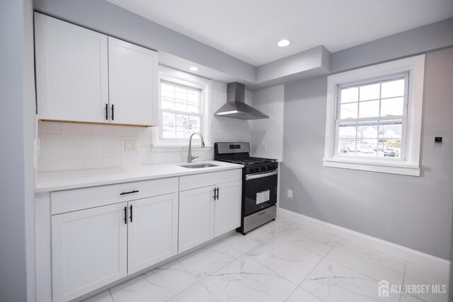 kitchen with sink, stainless steel range with gas cooktop, wall chimney range hood, decorative backsplash, and white cabinets