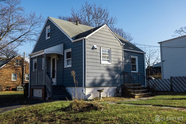 bungalow-style home featuring roof with shingles, a front yard, and fence