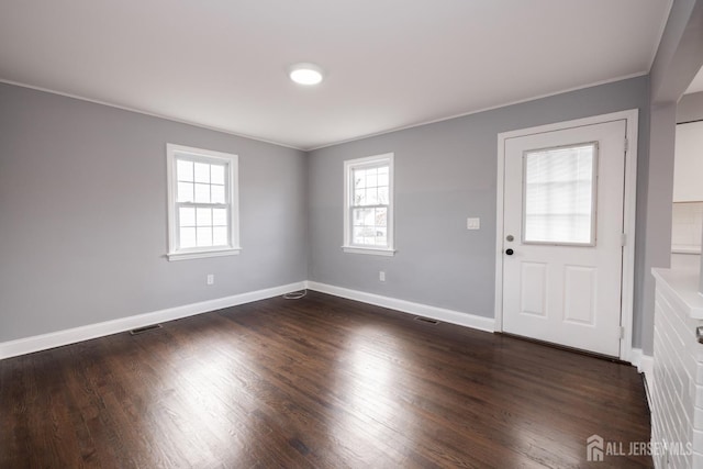 empty room featuring dark wood-style floors, visible vents, baseboards, and ornamental molding