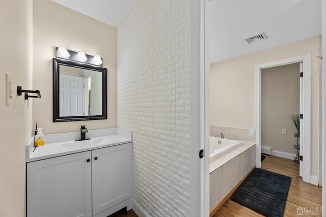 bathroom featuring hardwood / wood-style floors, a relaxing tiled tub, vanity, brick wall, and toilet