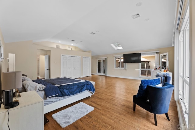 bedroom featuring hardwood / wood-style flooring, vaulted ceiling, and two closets