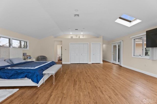 bedroom featuring two closets, vaulted ceiling with skylight, and light hardwood / wood-style floors