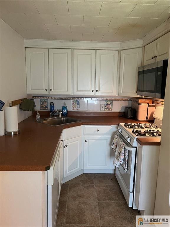 kitchen featuring white appliances, backsplash, sink, and white cabinets