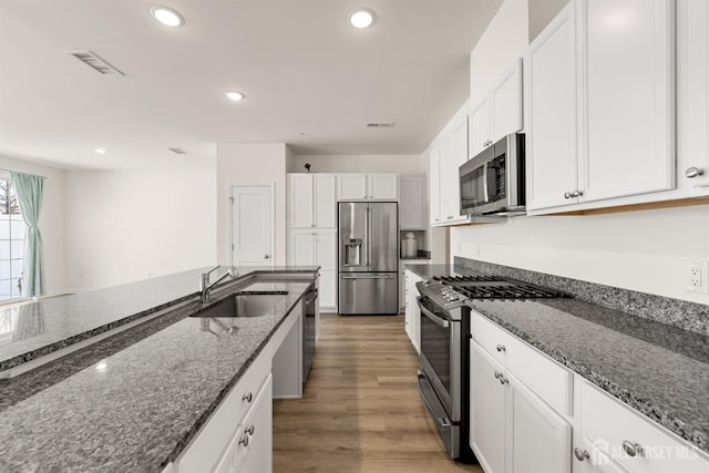kitchen with a sink, appliances with stainless steel finishes, dark stone countertops, and white cabinetry