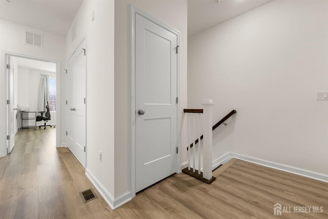 hall with visible vents, light wood-type flooring, and an upstairs landing