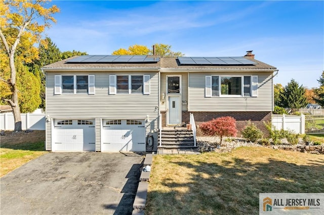 raised ranch with solar panels, a garage, and a front lawn