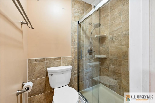 bathroom with a shower with door, toilet, and tile walls