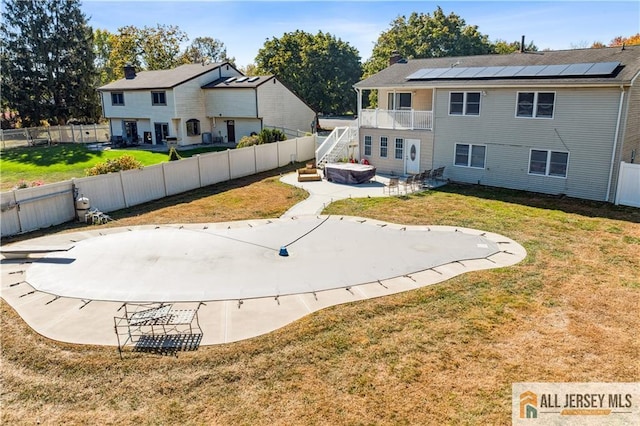 rear view of property featuring solar panels, a balcony, a patio area, and a lawn