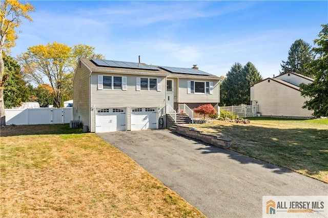 raised ranch with solar panels, central AC, a front yard, and a garage