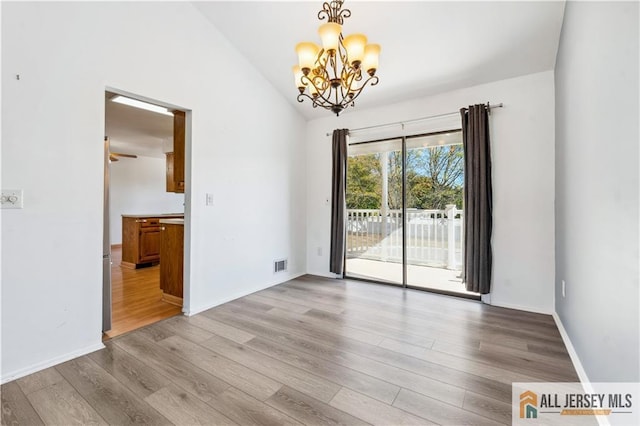 spare room featuring ceiling fan with notable chandelier, light hardwood / wood-style flooring, and lofted ceiling