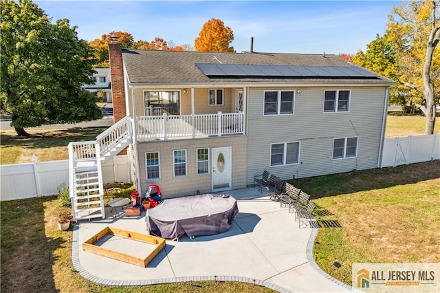 back of house featuring a lawn, solar panels, a patio area, and a balcony