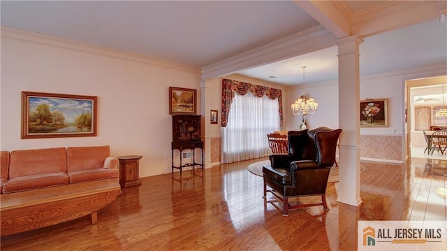 living area featuring decorative columns, crown molding, wood finished floors, and an inviting chandelier