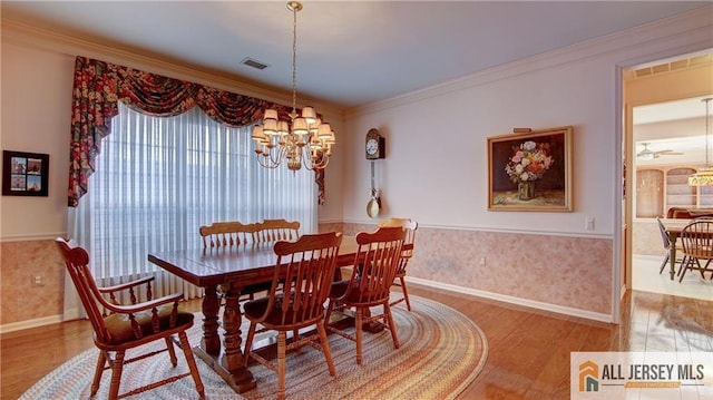 dining room with ornamental molding, wood finished floors, wainscoting, and an inviting chandelier