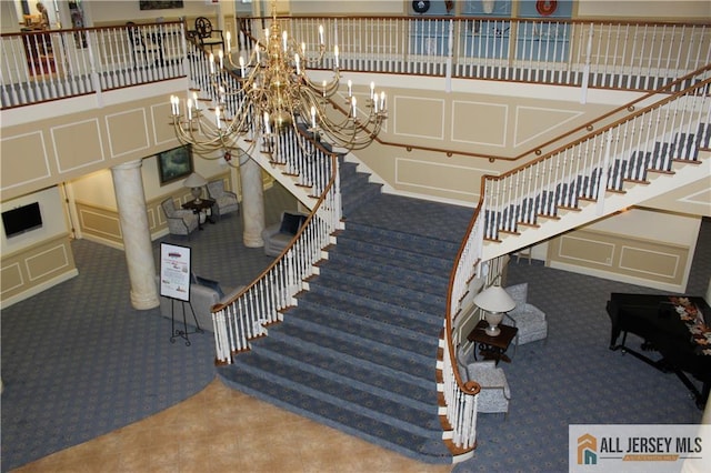 stairs with carpet flooring, a decorative wall, a chandelier, and decorative columns