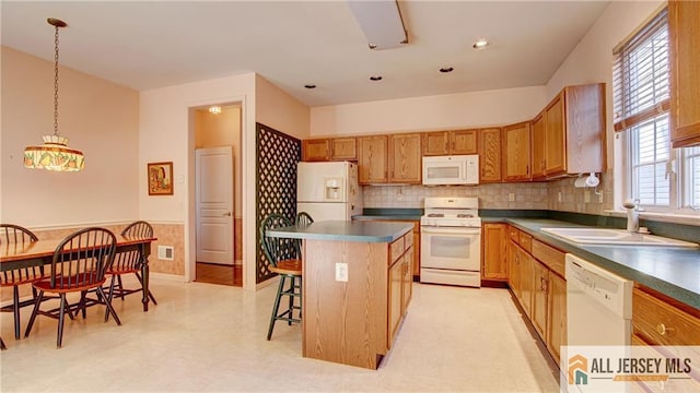 kitchen with dark countertops, a kitchen island, a sink, white appliances, and a kitchen breakfast bar