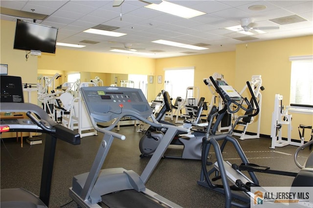 exercise room with a drop ceiling, a ceiling fan, and baseboards