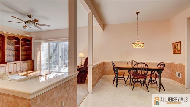 dining space featuring a wainscoted wall, a ceiling fan, visible vents, and wallpapered walls