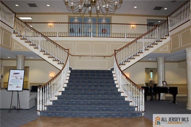 staircase with a high ceiling, an inviting chandelier, and ornate columns