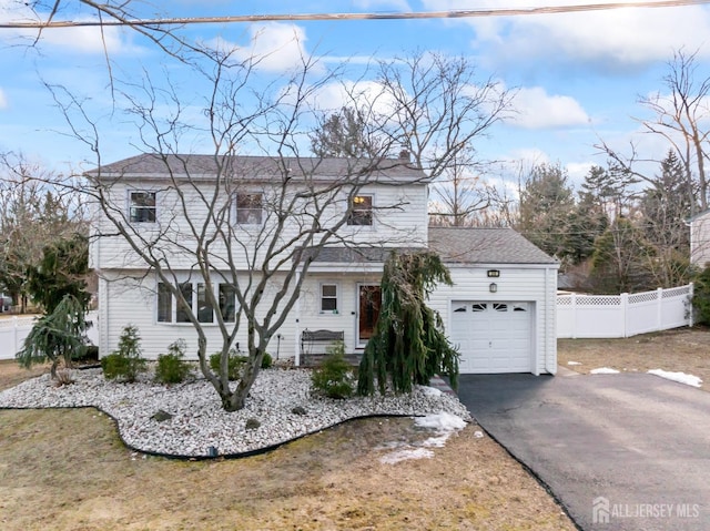 colonial house featuring aphalt driveway, fence, a shingled roof, and an attached garage