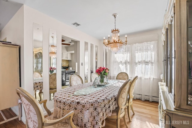 dining area with a chandelier, a baseboard heating unit, visible vents, and light wood-style floors