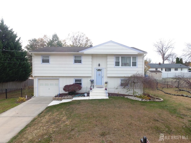 bi-level home featuring a garage, fence, concrete driveway, and a front yard