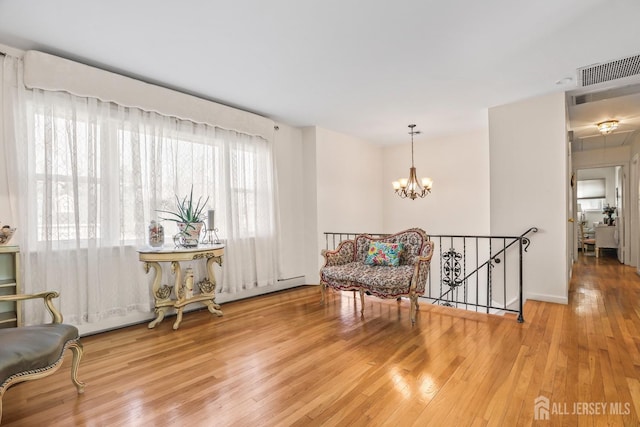 living area featuring visible vents, hardwood / wood-style floors, a chandelier, and an upstairs landing