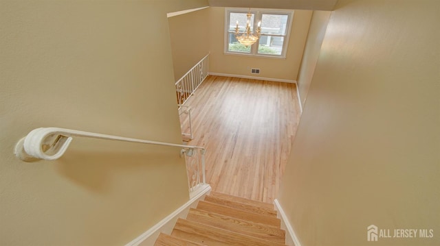 stairs featuring an inviting chandelier, wood finished floors, and baseboards