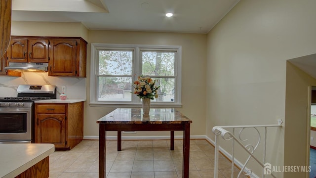 kitchen with stainless steel range with gas stovetop, under cabinet range hood, brown cabinets, light countertops, and recessed lighting