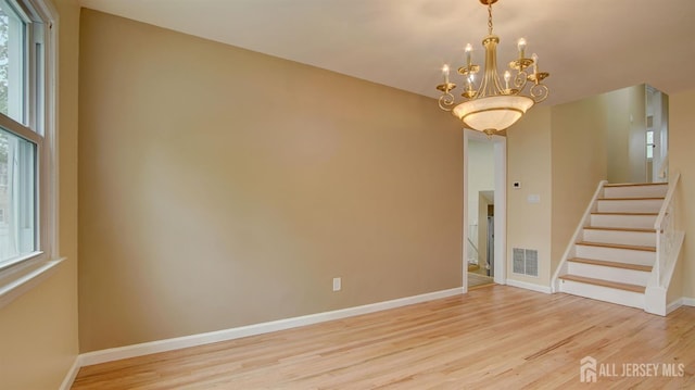 spare room featuring wood finished floors, stairs, a chandelier, and baseboards