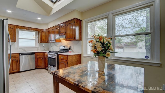 kitchen with light tile patterned floors, brown cabinets, under cabinet range hood, appliances with stainless steel finishes, and recessed lighting